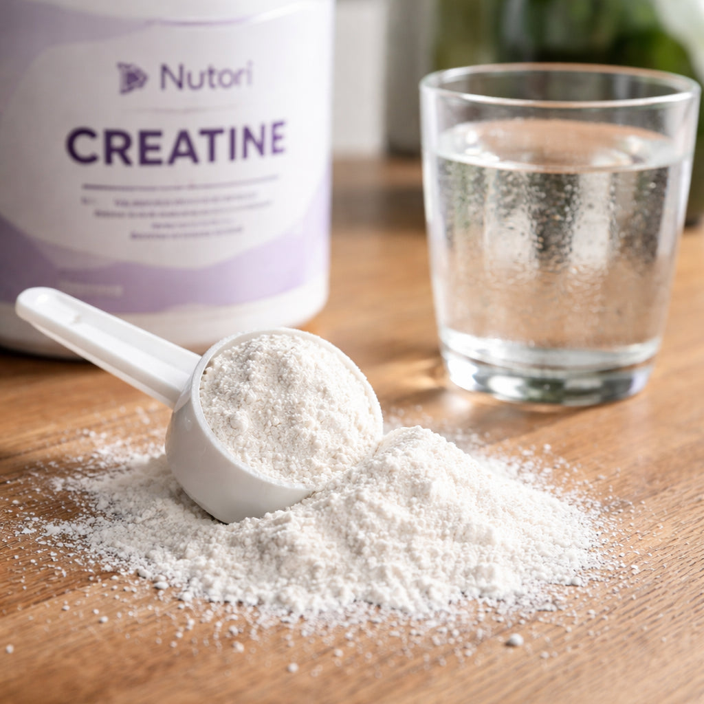 A realistic close‑up of a spoonful of white creatine monohydrate powder spilling onto a wooden surface, with a glass of water beside it. Alt: creatine powder dosage illustration